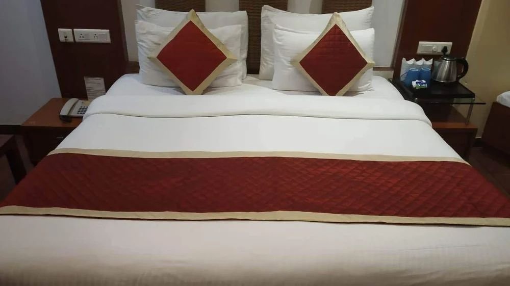 Hotel bed dressed with white linen and a maroon runner